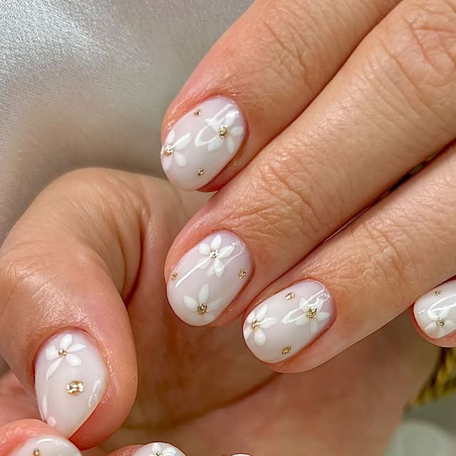 Nudefarbenes Nageldesign mit weißen Blüten und Goldakzent